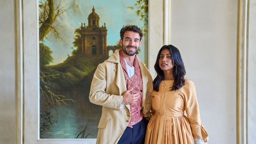 Ein Mann und eine eine Frau, die in historischen Kostümen gekleidet, lächeln in die Kamera