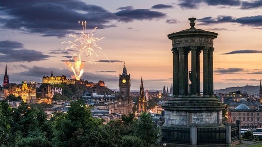 Fireworks at dusk in the sky over historic city monuments and castle.