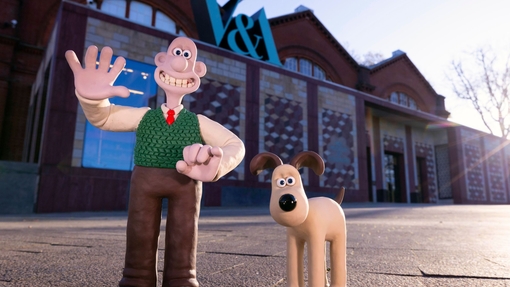 A clay character of a man waving outside a museum alongside a clay dog
