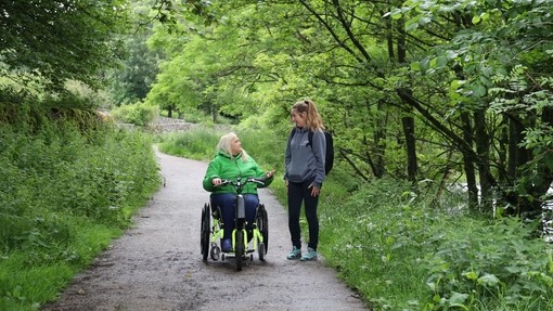 Zwei Frauen, eine mit einem Rollstuhl, auf einem Waldweg