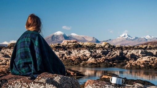 A woman sitting on a rock wrapped in a tartan blanket