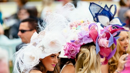 Royal Ascot Race Meeting at the prestigious Ascot racecourse in Berkshire. Young woman wearing a large white hat with feather and floral detail. Chatting to a friend.