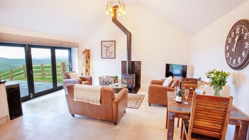 A living room with matching brown leather sofa and armchairs and a wood burner. 