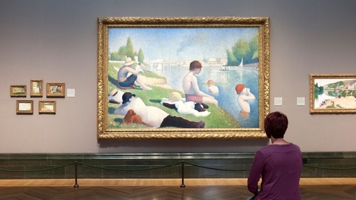 A woman, sitting in a gallery looking at a painting