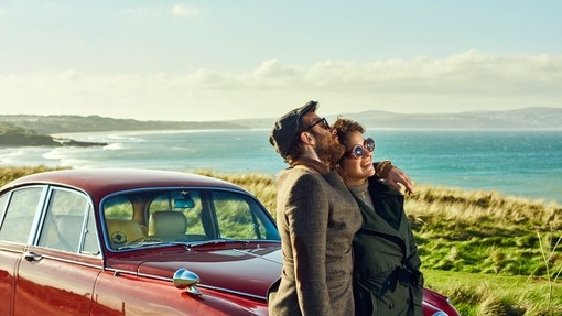 Couple cuddling in front of a red parked car. Smiling couple