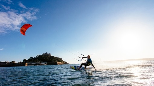 A man on a surfboard holding control bar of a kite canopy