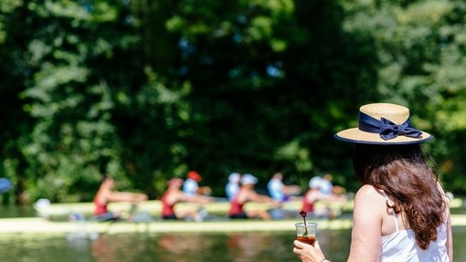 Woman wearing a hat drinking while watching a boat race