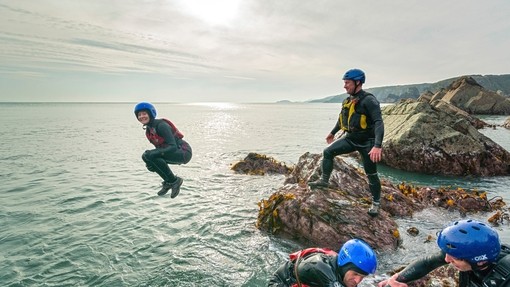 Four people in wet suits, helmets and life jackets on the coast
