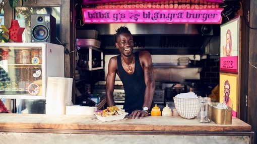 Smiling man working at food stall serving burgers