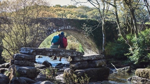 Couple sitting on stone bridge over stream