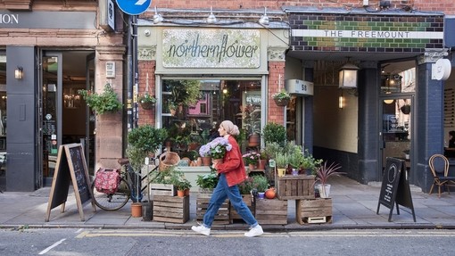 Woman holding bunch of flowers walking past boutique shops