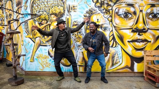 Two men standing in front of street art, dancing