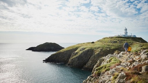 People walking on coastal path towards a lighthouse