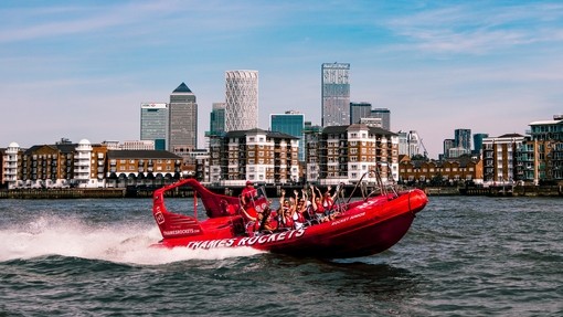 Passengers cheering on a red speed boat on river Thames in front of sky scrapers at Canary Wharf