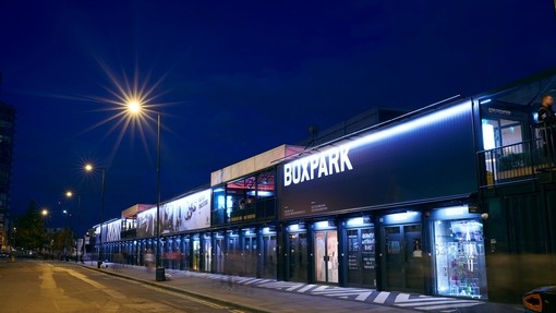 Exterior view of Boxpark, a pop-up mall in Shoreditch, London, at night.
