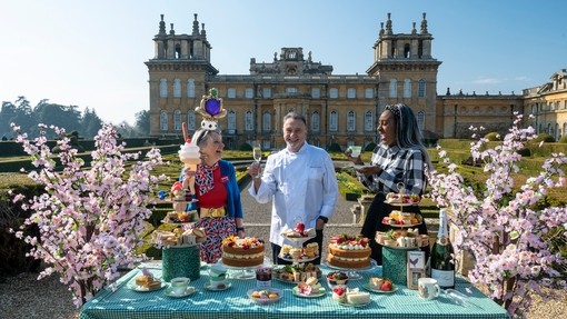 Chef and two guests stood at a display table in front of Blenheim Palace, with food and cakes on the table in front of them