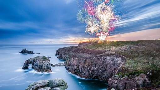 Firework display seen from across a rocky headland at twilight