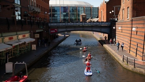 A group of people paddleboarding down a canal in the centre of Birmingham.