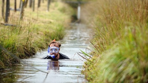 A competitor neck deep in a water-filled trench.