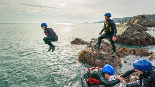 People coasteering off rocks into the ocean.