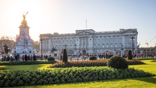 Vue du palais de Buckingham à Londres avec des jardins au premier plan et des gens qui se promènent.