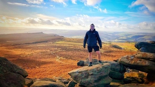 Ein Mann posiert auf dem Gipfel des Higger Tor mit einem weiten Blick auf den Peak District dahinter