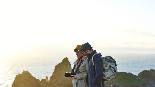 A couple standing on top of the cliffs. Man with backpack