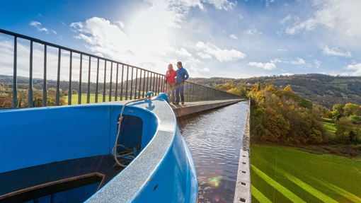 Couple walking along an Aqueduct in autumn with canal boat passing alongside.