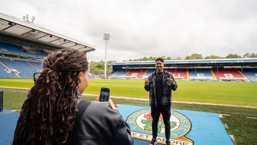 A woman takes a picture of a man at a football stadium