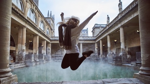 Woman leaping in the air at The Roman Baths, Bath, Somerset, England.