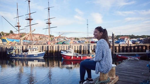 Femme souriante assise sur la jetée du port de Whitby, regardant les bateaux