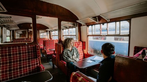 A man and a woman sitting at a table inside a train carriage.
