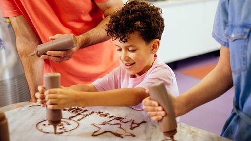 A boy, with curly hair, squeezing chocolate out of a bottle