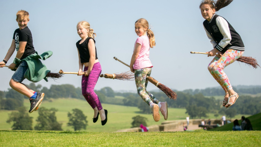 Four children demonstrate flying on a broom in the grounds of a castle.