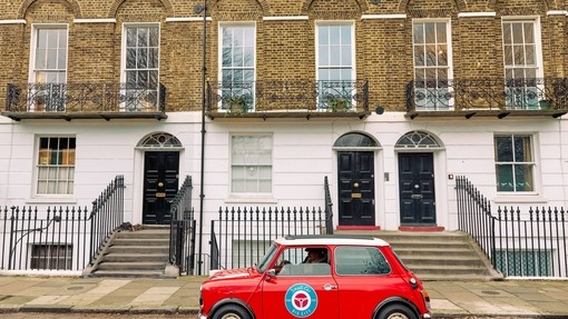 A red vintage car parked outside a row of Georgian townhouses