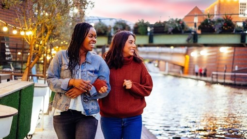 Two women, linking arms, walking beside a canal in evening