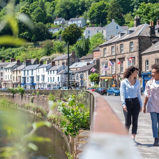 Two women walk down a main street in a hillside town