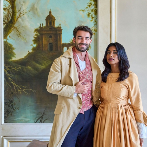 Ein Mann und eine eine Frau, die in historischen Kostümen gekleidet, lächeln in die Kamera