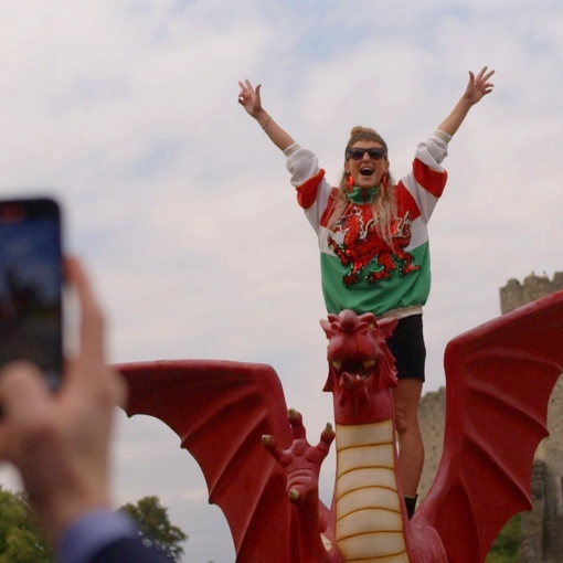 Woman has picture taken standing on a model Welsh dragon.