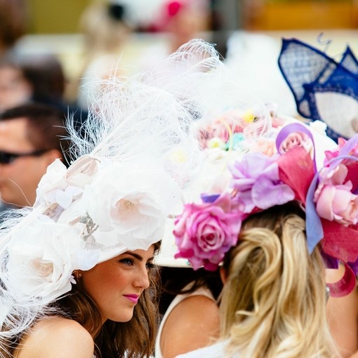 Junge Frau trägt einen großen weißen Hut mit Federn und Blumendetails beim Royal Ascot Race Meeting in Berkshire, England