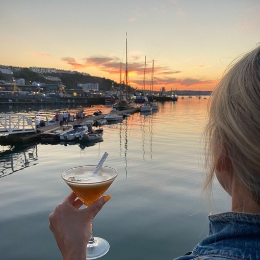 A woman holding a cocktail with view of Brixham harbour in distance.