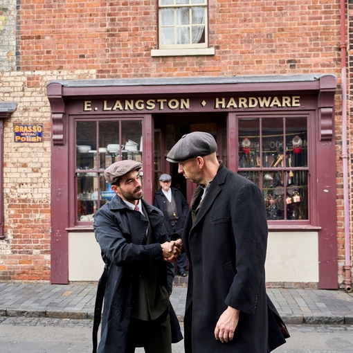 Two men shaking hands on the street in front a hardware shop at a living museum