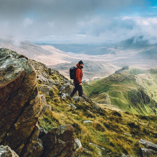 A rugged up man navigating the panoramic summit of a large mountain range