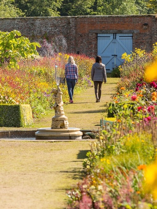 Two female friends walking through a formal garden
