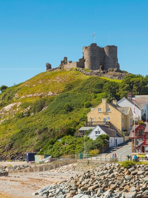 A castle on top of a hill beside a beach, surrounded by colourful buildings.