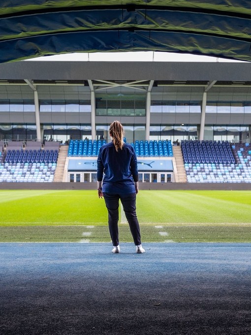 Woman standing in front of the pitch at the Manchester City Academy Stadium