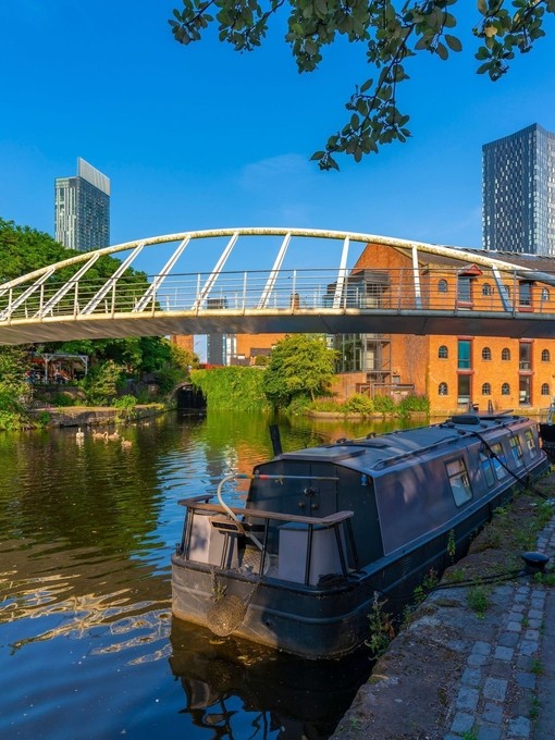 Canal boat moored on a canal with a pedestrian bridge and city buildings behind
