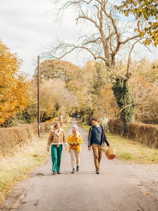Dos mujeres y un hombre caminando por un camino rural en otoño