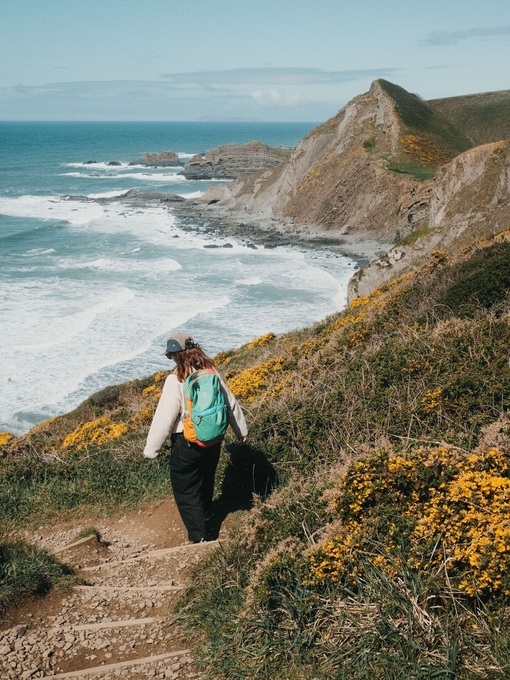 A woman walks along a coastal path with sea and headland in the distance