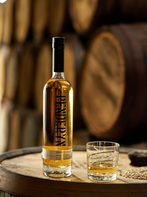 A bottle of whisky and a glass standing on an oak barrel